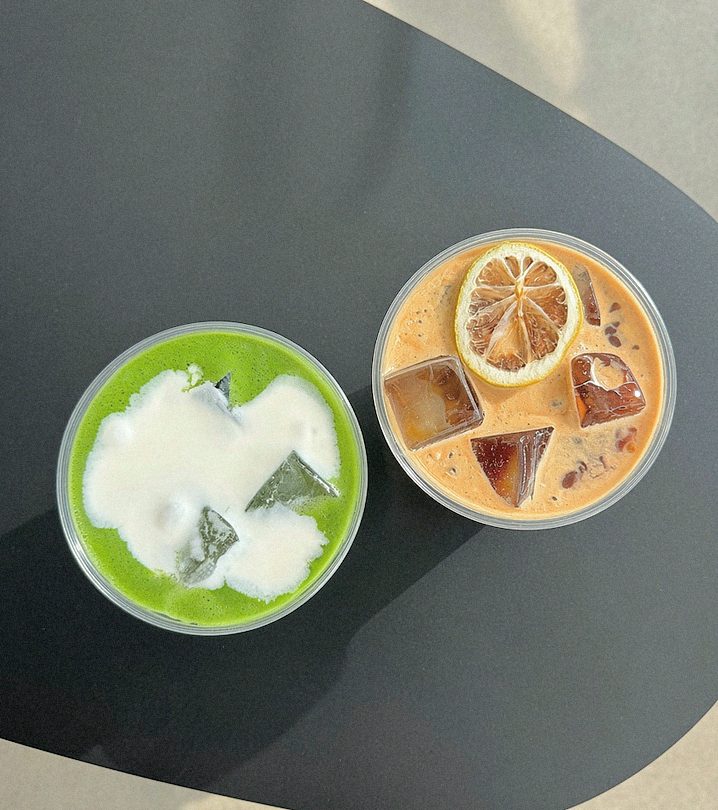 Iced matcha and iced coffee with lemon on a black table, seen from above.