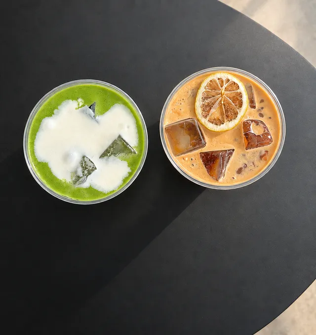 Iced matcha and iced coffee with a dried lemon slice, seen from above on a black table.