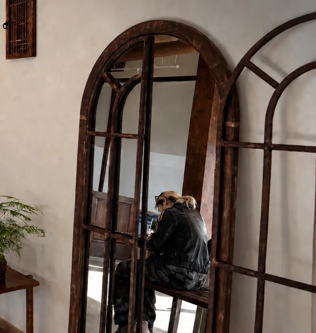 Arched dark-wood mirrors leaning against the warm plaster wall, a guest reflected in one.