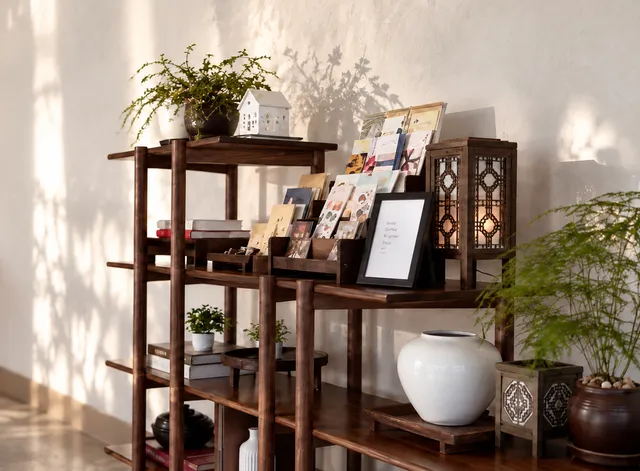 Walnut shelves with a white moon jar, postcards and a lattice lantern against a warm plaster wall.